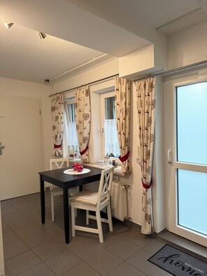 Ein Essbereich mit Tisch und Stühlen, ein Fenster mit Vorhängen und eine Tür mit Fußmatte.