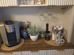 Eine Küchenzeile mit Kaffeemaschine, Torani-Sirup-Flaschen, einem Keurig-Kaffeemaschine, einer Topfpflanze, einem Kaffeemühle und einer Tasse mit Besteck.