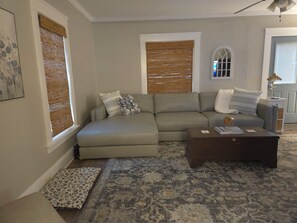 Ein Wohnzimmer mit einem Ecksofa, einem Couchtisch und einem gemusterten Teppich.