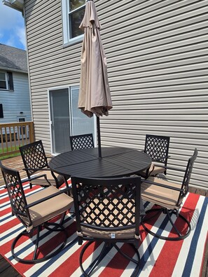 Eine Terrasse mit rundem Tisch und Stühlen, einem Sonnenschirm und Blick auf ein Haus.