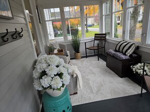 Een zonnedak met een witte vloer, een bank met decoratieve kussens, een stoel, een potplant en een decoratieve wand met haken.
