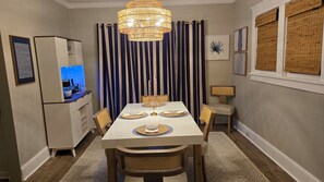 A dining area with a table set for four, a chandelier, striped curtains, and a refrigerator with a lit display. - Cozy renovated century home retreat minutes away from Lake Erie. (Conneaut)