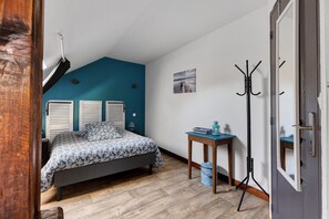 A bedroom with a bed, a small table, a coat rack, and a picture on the wall. - Chambre Bleue, Table d'Hôte with Terrace, Shared Garden & Wi-Fi (Fursac)