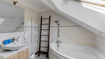 A modern bathroom with a freestanding bathtub, a wooden ladder, a white sink with blue cups, and a large mirror.
