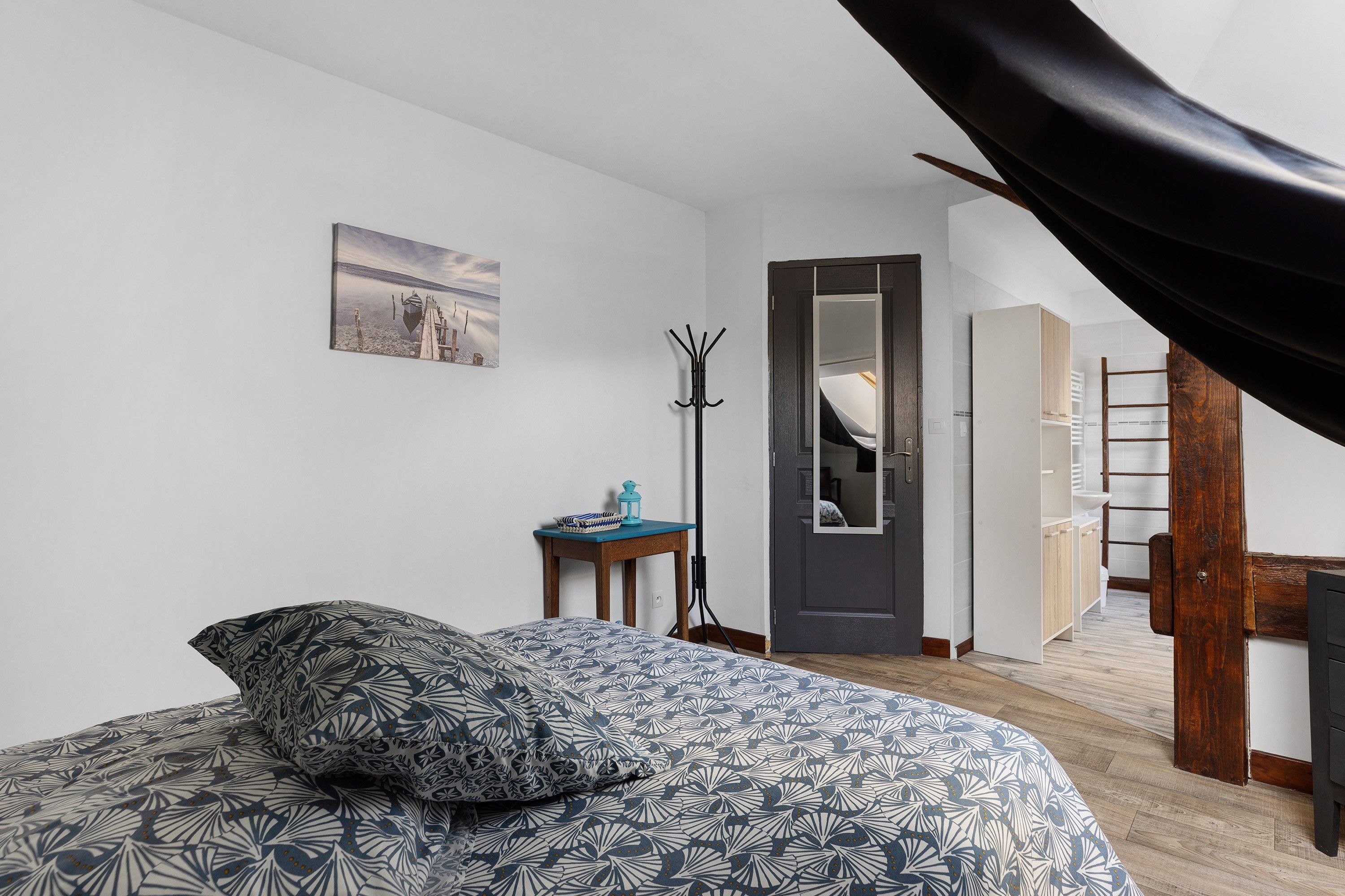 Een slaapkamer met een bed, een kapstok, een deur en uitzicht op een gang.