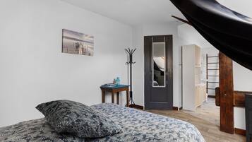 Een slaapkamer met een bed, een kapstok, een deur en uitzicht op een gang.