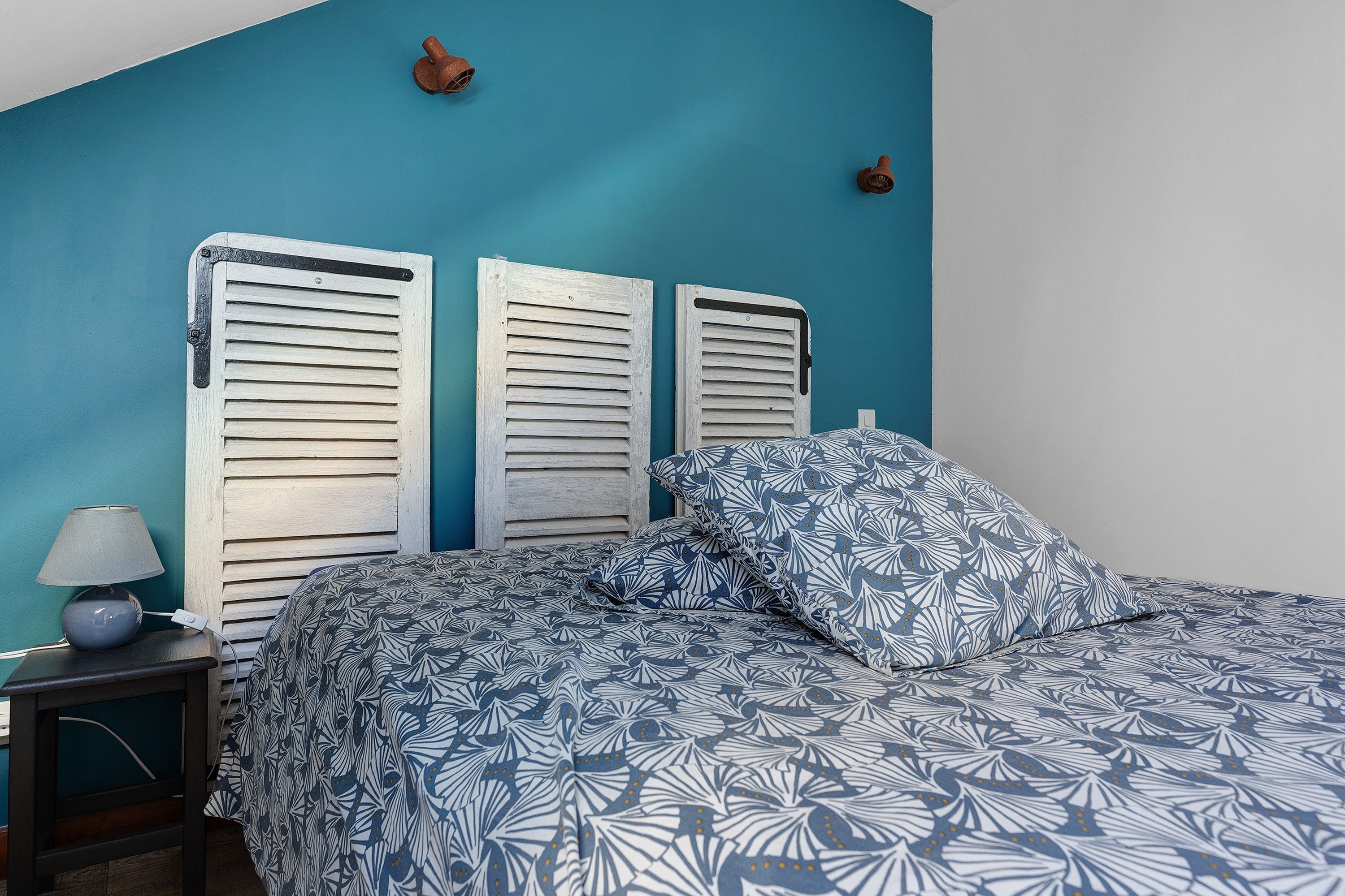A bedroom with a bed, a nightstand, a lamp, and a wall with two decorative items.