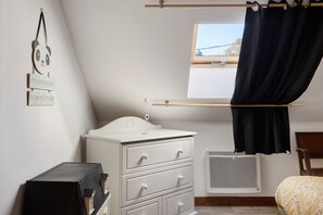 A bedroom with a white dresser, a window with black curtains, a radiator, and a wall-mounted decoration.