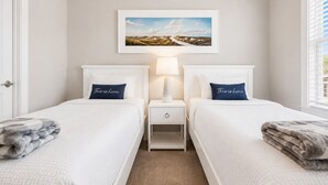 Une chambre d’hôtel avec deux lits, une table de chevet avec une lampe, un tableau représentant un paysage accroché au mur et une vue sur l’extérieur par la fenêtre.