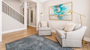 Un salon moderne avec un escalier, deux fauteuils, une lampe sur pied et un grand tableau abstrait.