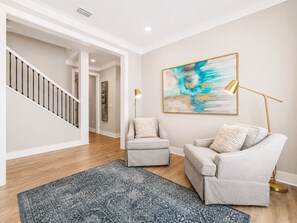 A modern living room with a staircase, two armchairs, a floor lamp, and a large abstract painting. - The Sandpiper Hideaway (Panama City Beach)