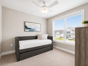 A bedroom with a bed, a ceiling fan, a window with blinds, and a view of a house outside. - The Sandpiper Hideaway (Panama City Beach)