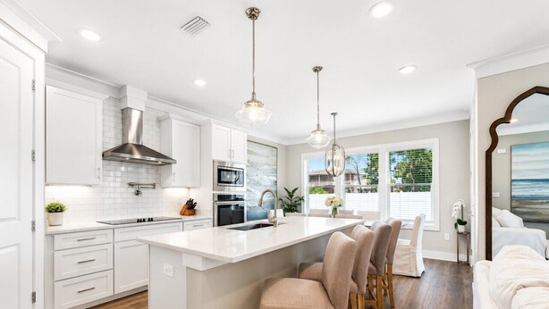 Une cuisine moderne avec des meubles blancs, un îlot central et des luminaires suspendus.