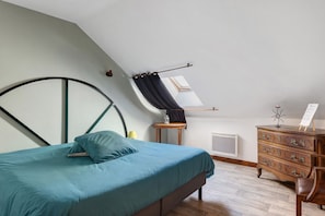 A bedroom with a bed, a dresser, a radiator, and a window with curtains.