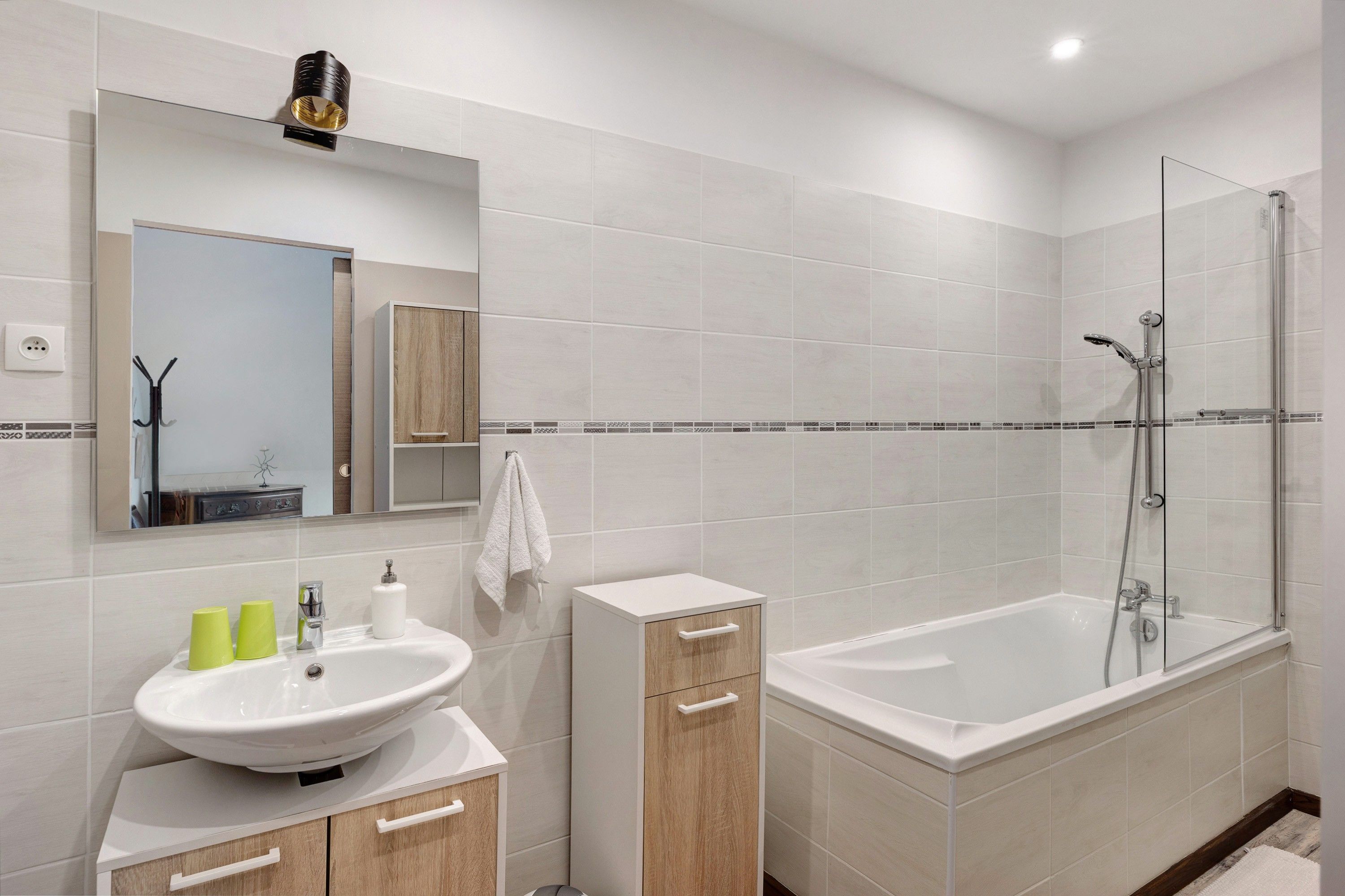 A modern bathroom with a white sink, wooden cabinet, and a glass-enclosed shower.
