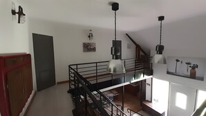Un interior de varios niveles con una escalera, iluminación colgante y obras de arte en las paredes.