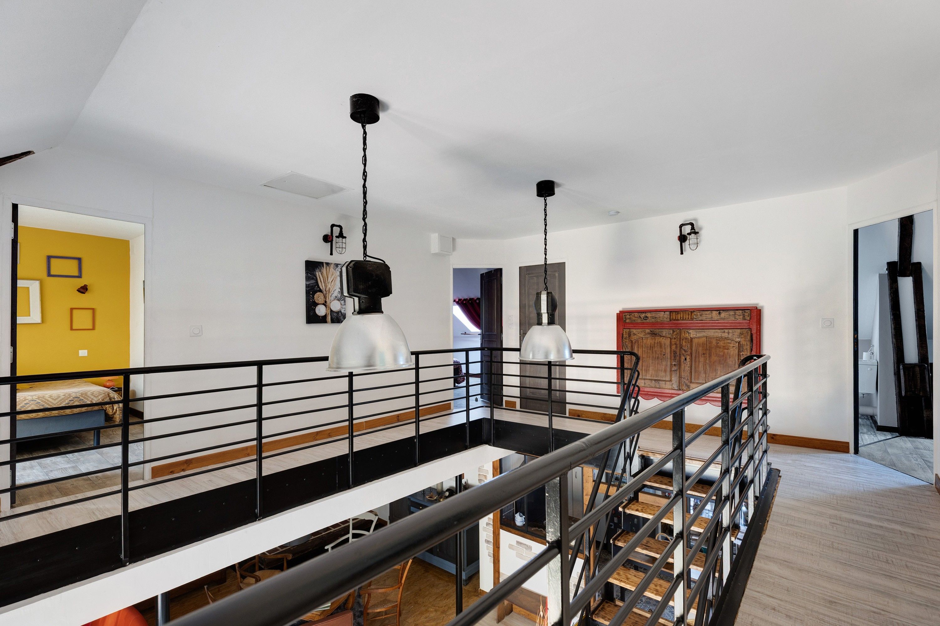 Un intérieur moderne aux couleurs contrastées, en noir et blanc, avec un escalier doté de rampes en métal, une porte jaune et un meuble rouge.