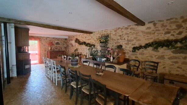 Un comedor con una larga mesa de madera, varias sillas y una pared de piedra.
