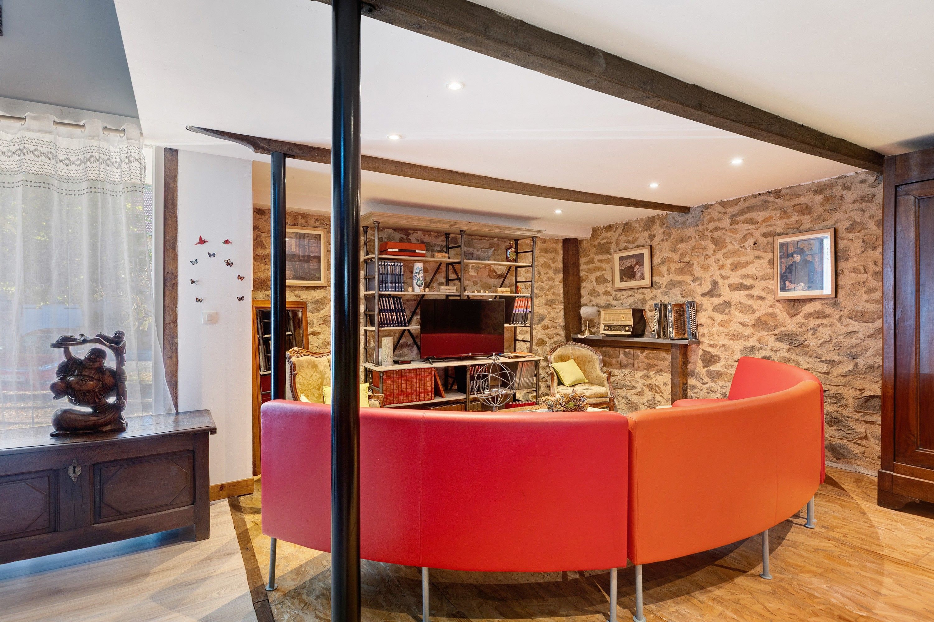 A living room with a curved red sofa, a wooden coffee table, and a bookshelf filled with books and decorative items.
