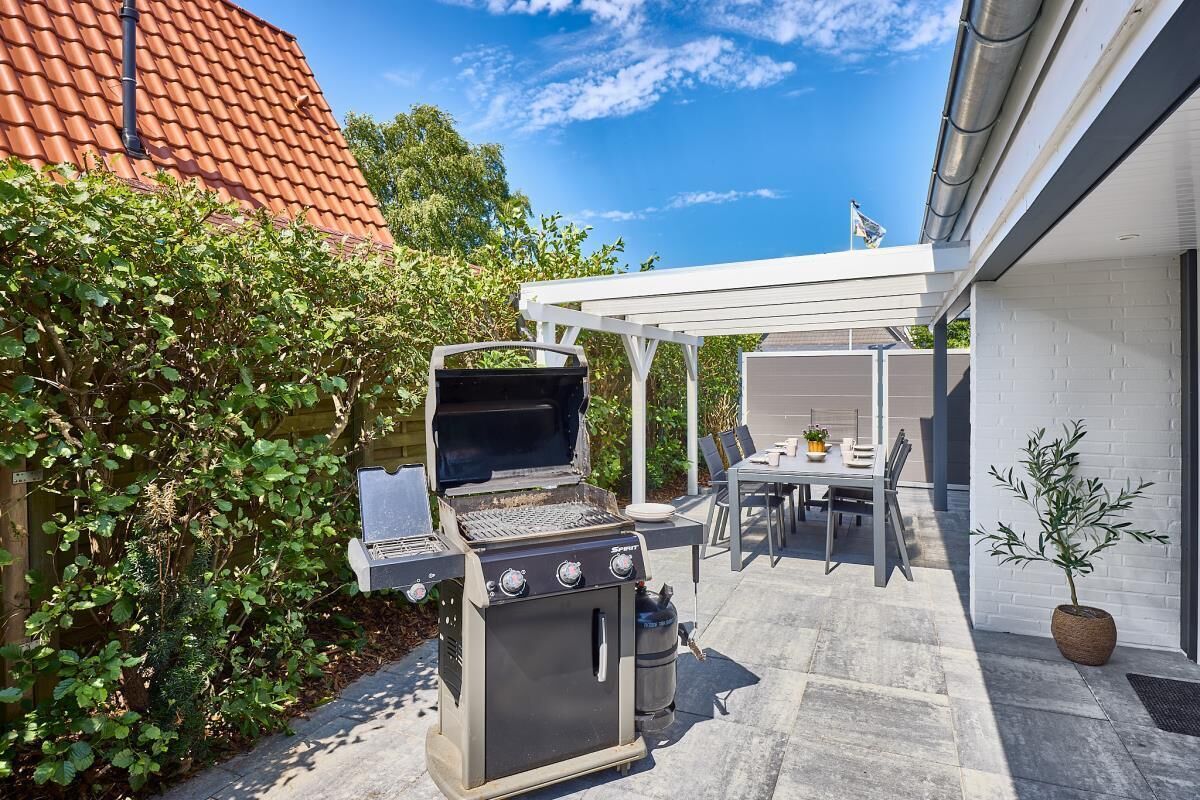 An outdoor patio with a grill, dining table, and chairs.