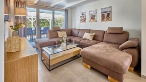 A modern living room with a sectional sofa, a glass coffee table, and a view of the outdoors through large windows. - Vacation Home at Am Ringwal 82 in Cuxhaven Duhnen—modernized in 2026 with a Wallbox (Cuxhaven)