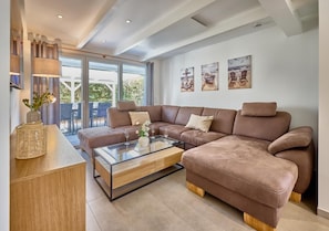 A modern living room with a sectional sofa, a glass coffee table, and a view of the outdoors through large windows. - Vacation Home at Am Ringwal 82 in Cuxhaven Duhnen—modernized in 2026 with a Wallbox (Cuxhaven)