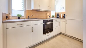 A modern kitchen with white cabinetry, a built-in oven, and a window providing natural light. - Vacation Home at Am Ringwal 82 in Cuxhaven Duhnen—modernized in 2026 with a Wallbox (Cuxhaven)