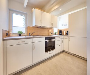 A modern kitchen with white cabinetry, a built-in oven, and a window providing natural light. - Vacation Home at Am Ringwal 82 in Cuxhaven Duhnen—modernized in 2026 with a Wallbox (Cuxhaven)