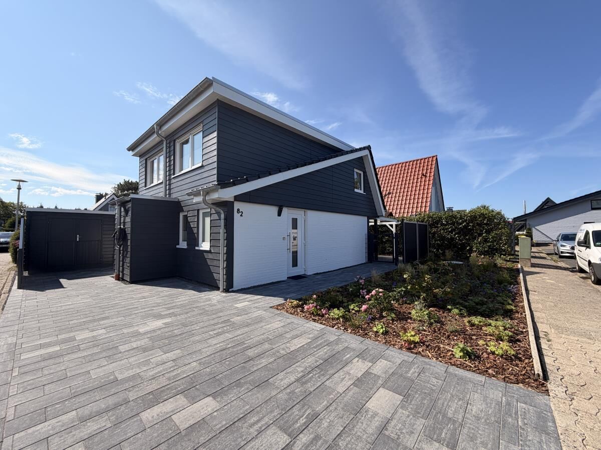 A two-story residential building with a garage, a driveway, and a small garden area.