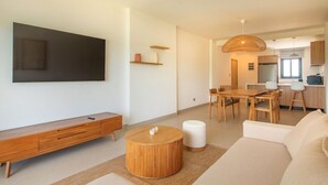 A modern living room with a flat-screen TV, wooden furniture, a round coffee table, and a dining area with a wooden table and chairs. - Born | Family Getaway with Pool View (Bavaro)