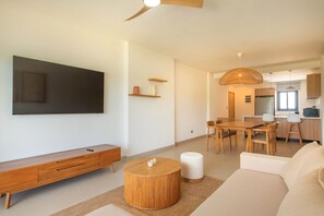 A modern living room with a flat-screen TV, wooden furniture, a round coffee table, and a dining area with a wooden table and chairs. - Born | Family Getaway with Pool View (Bavaro)
