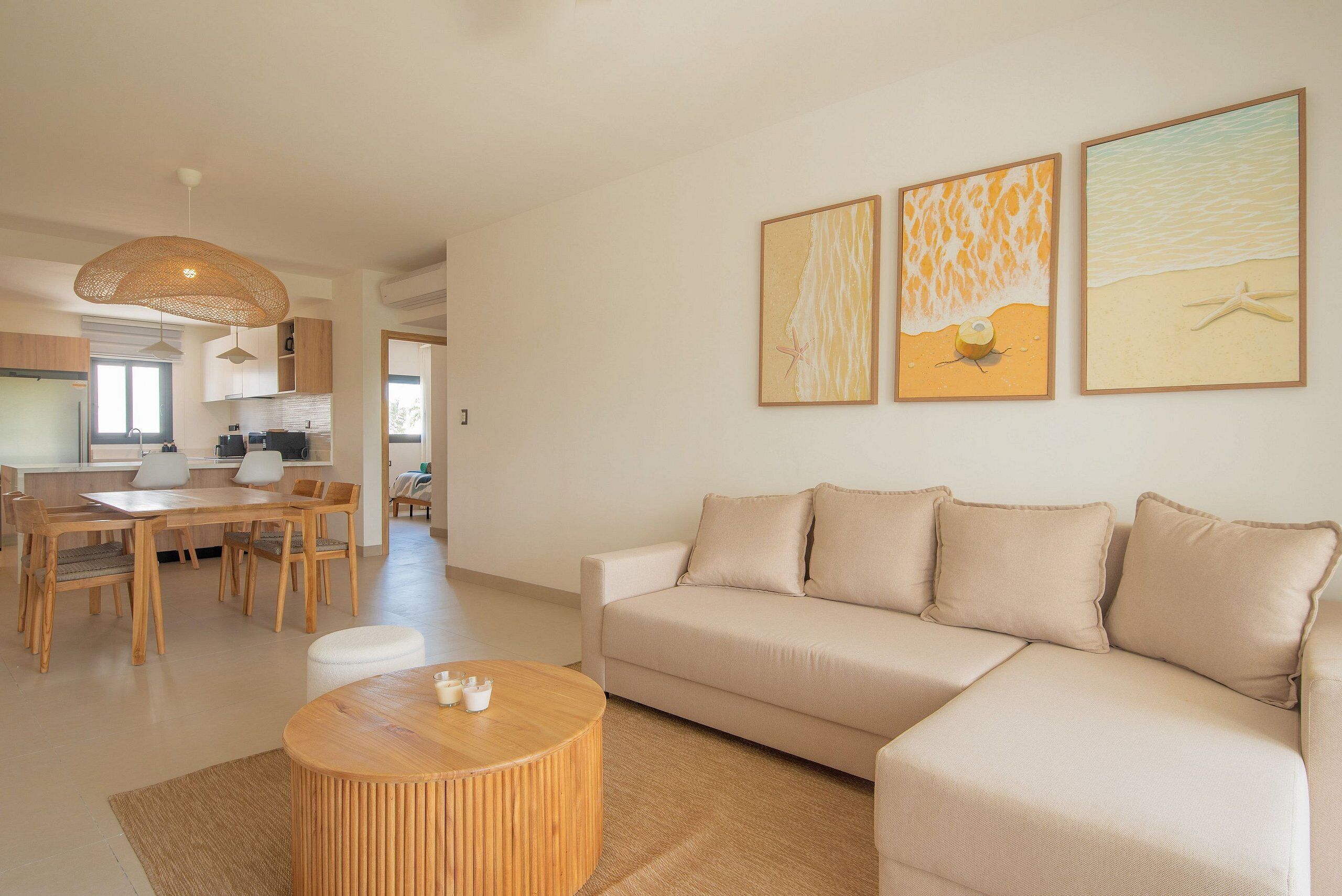 Un salon moderne avec un canapé, une table basse ronde en bois et un coin repas comprenant une table et des chaises. Trois œuvres d’art encadrées ornent le mur.