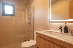 A modern bathroom with a glass shower enclosure, a toilet, a sink with a mirror, and a bottle of soap. - Born | Family Getaway with Pool View (Bavaro)