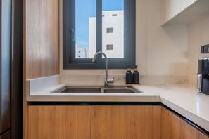 A kitchen with a double sink, wooden cabinets, a window, and a view of buildings outside. - Born | Family Getaway with Pool View (Bavaro)