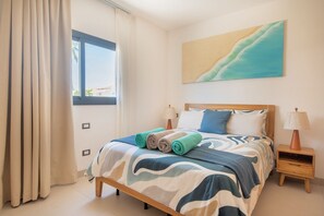 A hotel room with a bed, a nightstand, a lamp, a painting, and a window with curtains. - Born | Family Getaway with Pool View (Bavaro)
