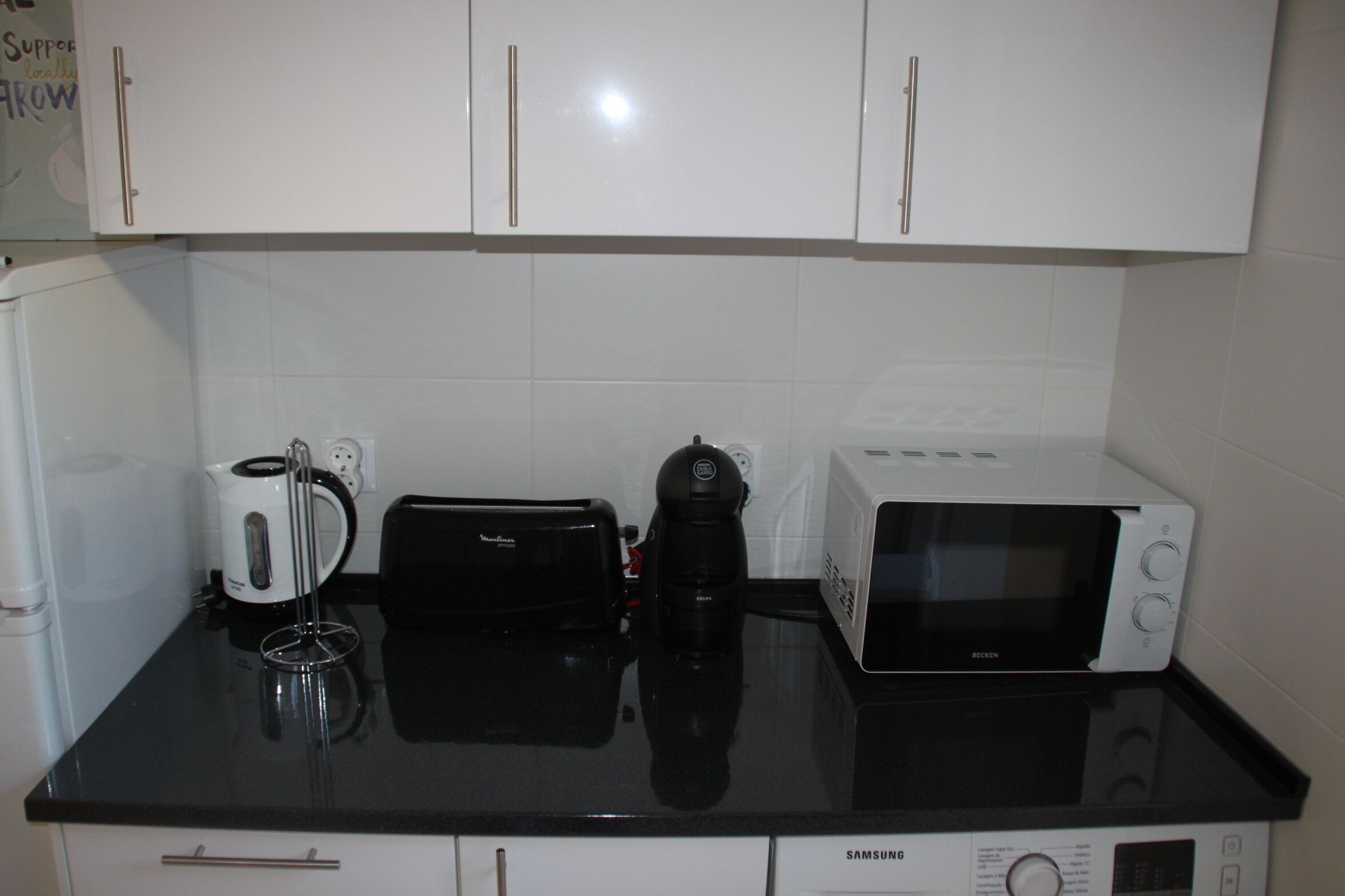 A kitchen with white cabinets, a black countertop, a coffee maker, a toaster, and a microwave.