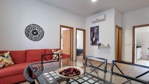Uma sala de estar moderna com uma mesa de centro de vidro, sofá vermelho e uma peça decorativa na parede.