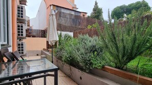 Um pátio com mesa e cadeiras de vidro, cerca de madeira e diversas plantas.
