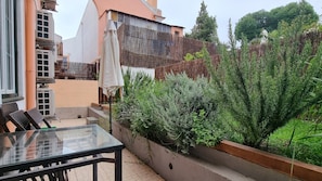 Eine Terrasse mit einem Glastisch und Stühlen, einem Holzzaun und verschiedenen Pflanzen.