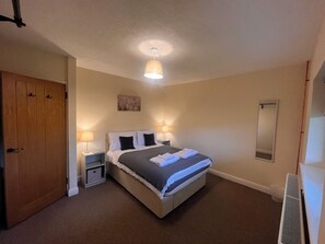 A hotel room with a bed, bedside lamps, a door, a small table, and a wall-mounted mirror. - Saddleback Bungalow (Llandrindod Wells)
