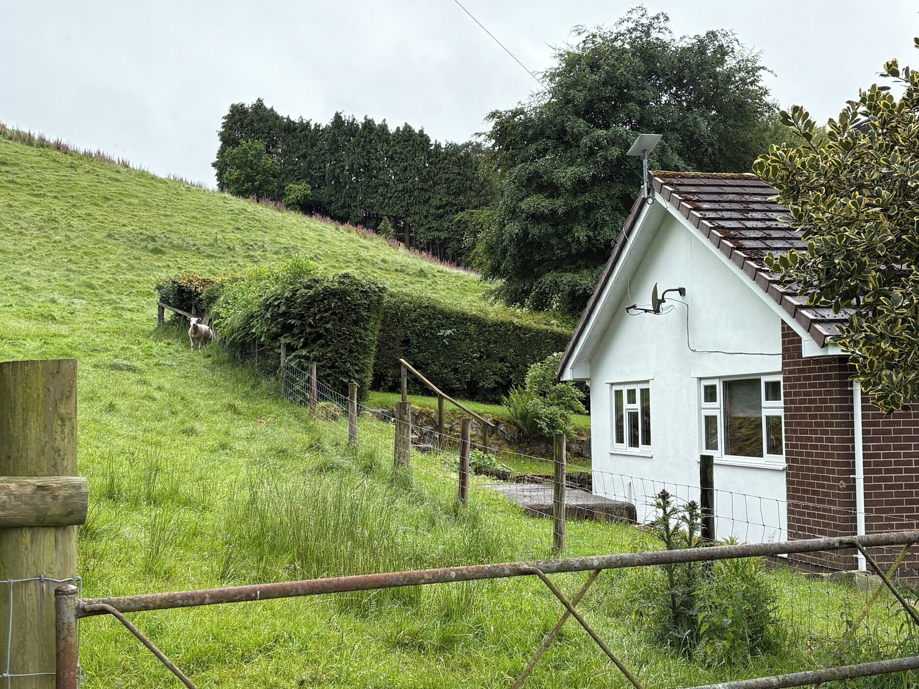 Een wit huis met schuine dak, omringd door een grasheuvel en een hek.