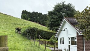 Ein weißes Haus mit geneigtem Dach, umgeben von einer grasbewachsenen Hügellandschaft und einem Zaun.
