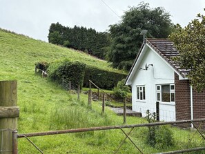 Ein weißes Haus mit geneigtem Dach, umgeben von einer grasbewachsenen Hügellandschaft und einem Zaun.
