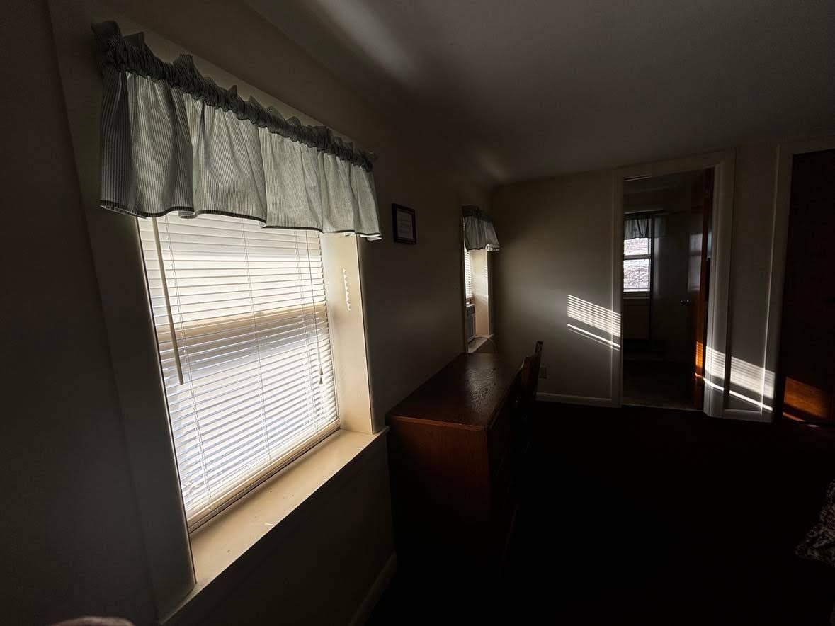 A room with a window, a wooden bench, and a door leading to another room.