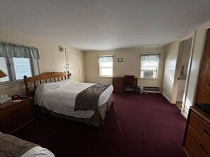 Un dormitorio con una cama grande, un escritorio y una silla. Hay dos ventanas con cortinas.