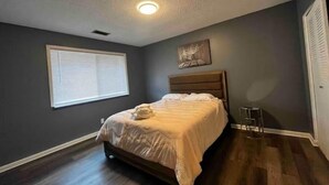 A bedroom with a bed, a window, a ceiling light, and a nightstand.