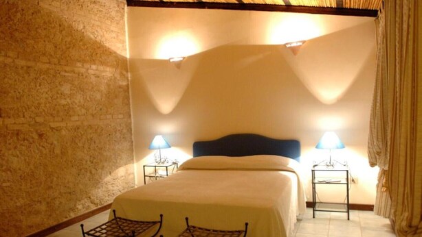 A room with a bed, two bedside tables with lamps, a chair, and a brick wall. - Room 'Il Pero Selvatico, Doppia' with Shared Garden, Wi-Fi and Air Conditioning (Roccelletta)