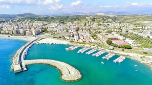 A coastal cityscape with a marina, residential buildings, and a curved breakwater.