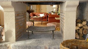Una chimenea de piedra con un banco delante, un sofá de cuero rojo y una mesita con una lámpara.