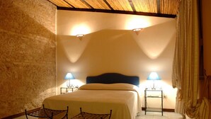 Un dormitorio con una cama, dos mesitas de noche con lámparas, una silla y un techo de madera.